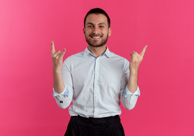 Sorridente uomo bello gesti corna mano segno isolato sulla parete rosa