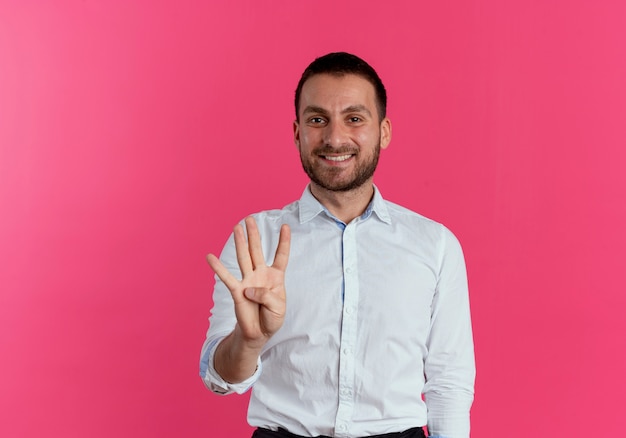 Sorridente uomo bello gesti quattro con la mano isolata sulla parete rosa