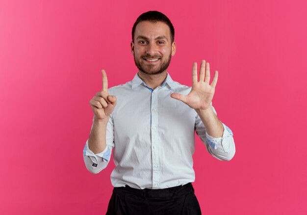 Sorridente uomo bello gesti sei con le mani isolate sulla parete rosa