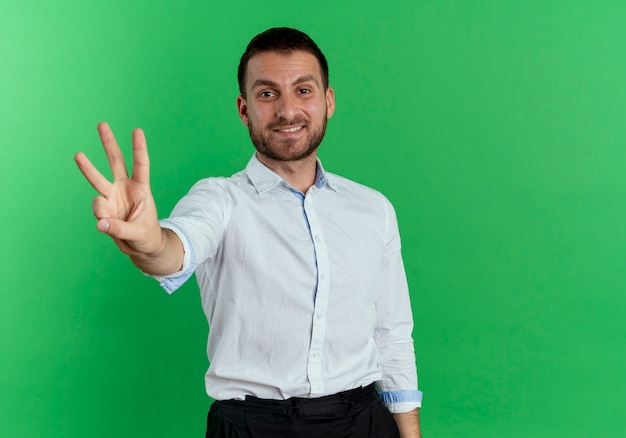 Sorridente uomo bello gesti tre isolati sulla parete verde