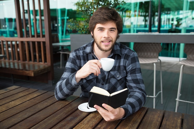 Sorridente uomo bere caffè e leggere il diario in street cafe