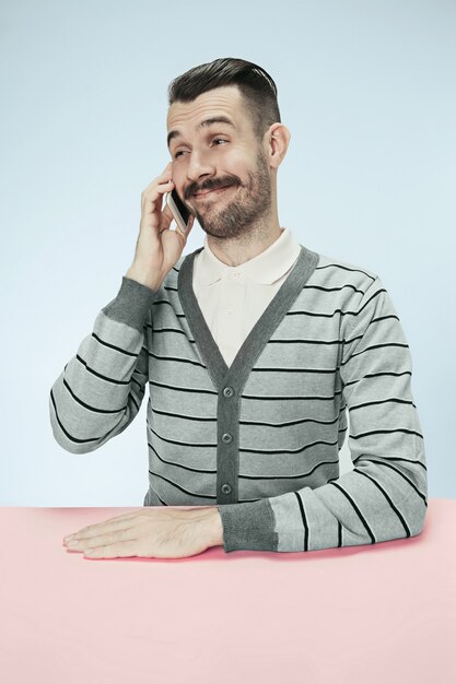 Sorridente uomo d'affari felice parlando al telefono seduto al tavolo. Concetto di emozioni maschili