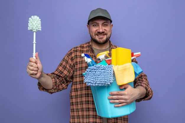 Sorridente uomo delle pulizie che tiene in mano attrezzature per la pulizia e scopino per la toilette