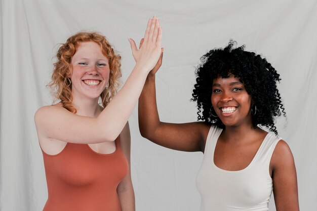 Sorridenti giovani donne africane e bionde che danno il livello cinque contro il contesto grigio
