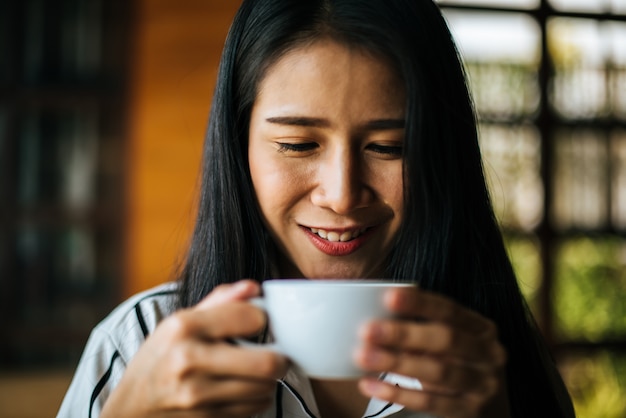 Sorridere asiatico della donna del ritratto si rilassa nel caffè della caffetteria