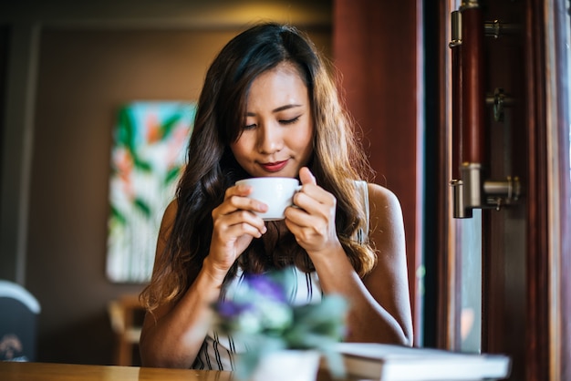 Sorridere asiatico della donna del ritratto si rilassa nel caffè della caffetteria