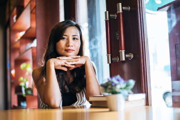 Sorridere asiatico della donna del ritratto si rilassa nel caffè della caffetteria