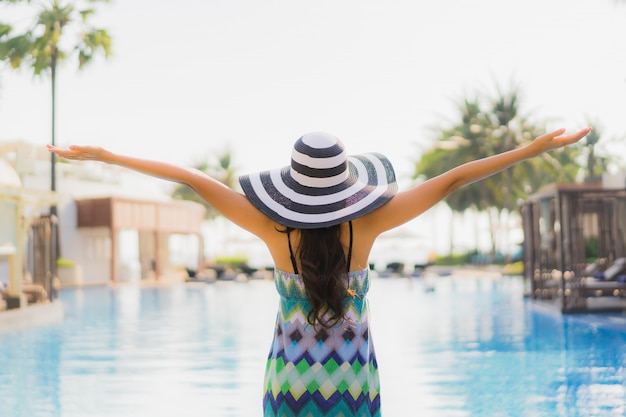 Sorrisi felici della bella giovane donna asiatica del ritratto e si rilassano intorno alla piscina nella località di soggiorno dell&#39;hotel