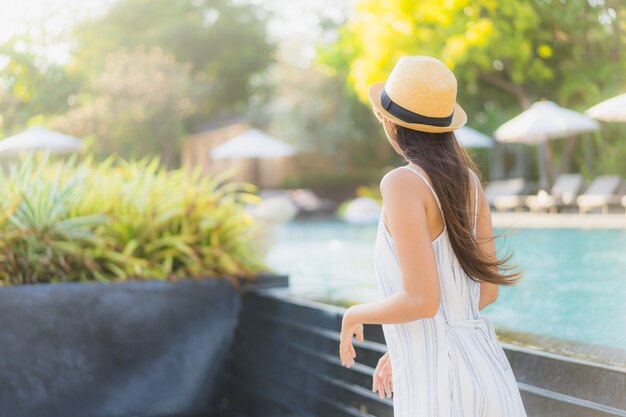 Sorrisi felici della bella giovane donna asiatica del ritratto e si rilassano intorno alla piscina nella località di soggiorno dell&#39;hotel