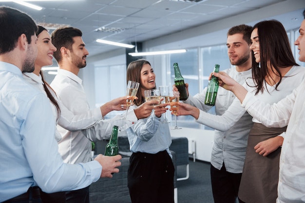 Sorrisi sinceri. In piedi e bussando a bottiglie e bicchiere. In ufficio. I giovani celebrano il loro successo