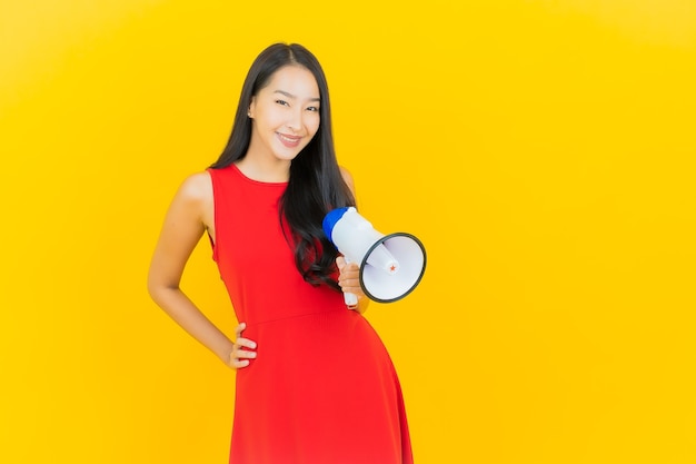 Sorriso della bella giovane donna asiatica del ritratto con il megafono sulla parete gialla