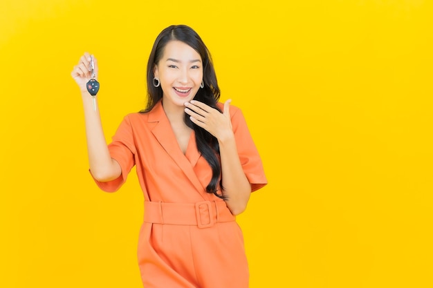 Sorriso della bella giovane donna asiatica del ritratto con la chiave dell'automobile su colore giallo
