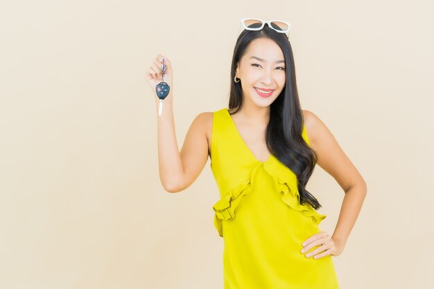 Sorriso della bella giovane donna asiatica del ritratto con la chiave dell'automobile sulla parete di colore