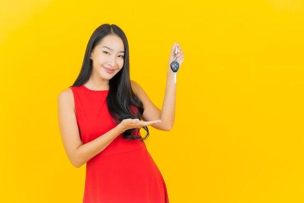 Sorriso della bella giovane donna asiatica del ritratto con la chiave dell'automobile sulla parete gialla