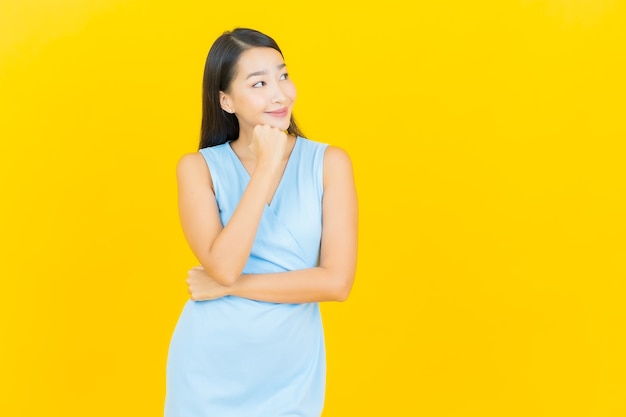 Sorriso di bella giovane donna asiatica del ritratto con azione sulla parete di colore giallo