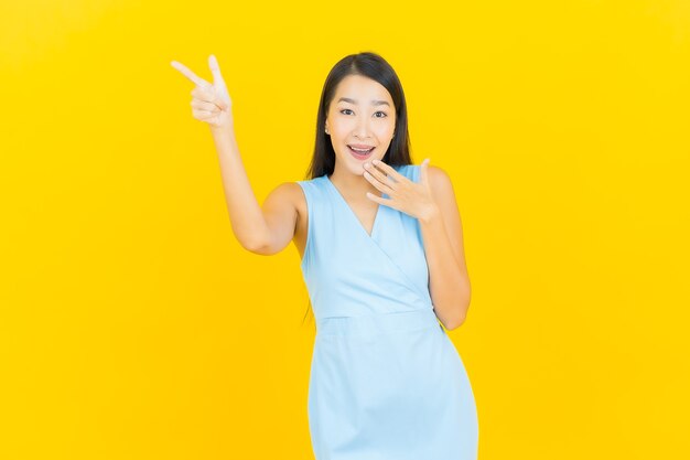 Sorriso di bella giovane donna asiatica del ritratto con azione sulla parete di colore giallo