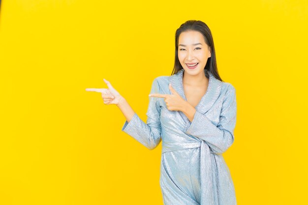 Sorriso di bella giovane donna asiatica del ritratto con azione sulla parete gialla