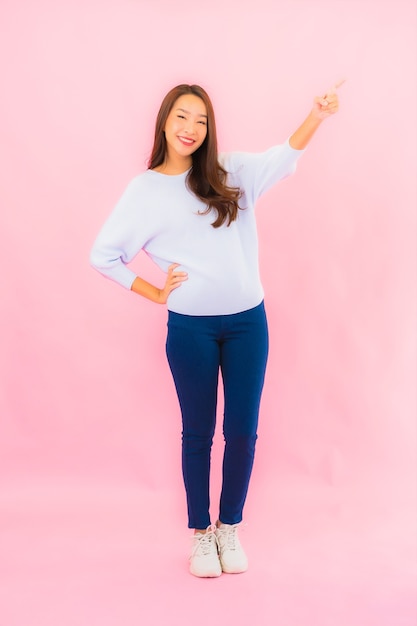 Sorriso di bella giovane donna asiatica del ritratto con azione sulla parete isolata rosa