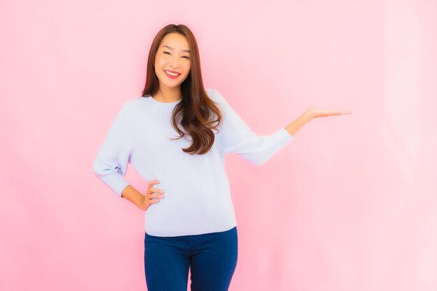 Sorriso di bella giovane donna asiatica del ritratto con azione sulla parete isolata rosa