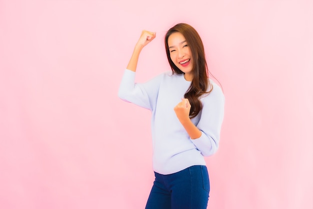 Sorriso di bella giovane donna asiatica del ritratto con azione sulla parete isolata rosa