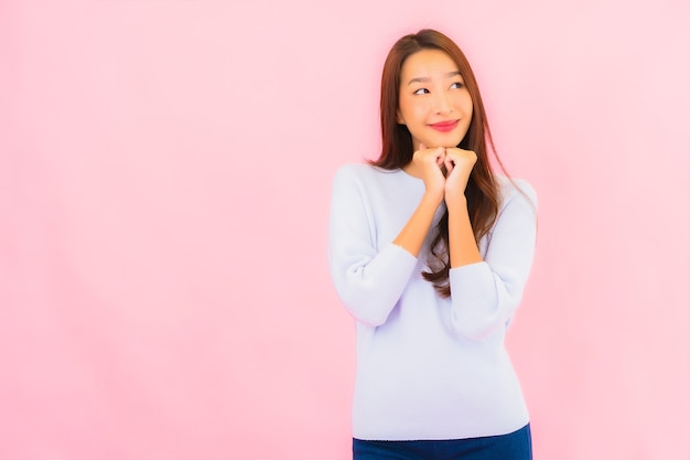 Sorriso di bella giovane donna asiatica del ritratto con azione sulla parete isolata rosa