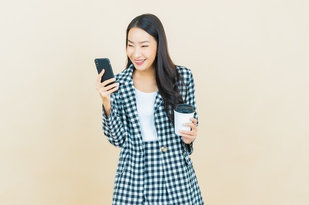 Sorriso di bella giovane donna asiatica del ritratto con il telefono cellulare astuto su beige