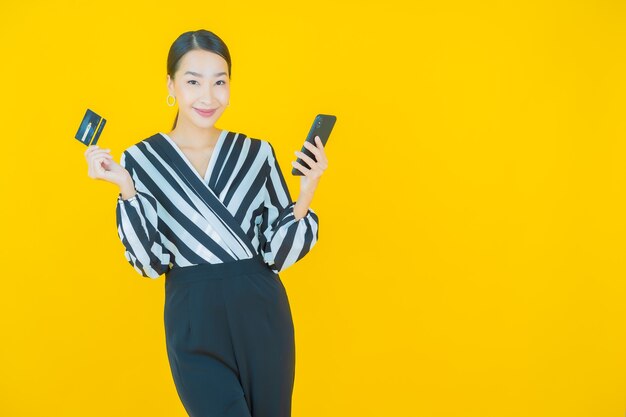 Sorriso di bella giovane donna asiatica del ritratto con il telefono cellulare astuto su yellow