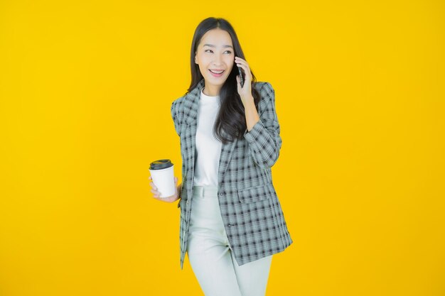 Sorriso di bella giovane donna asiatica del ritratto con il telefono cellulare astuto sul fondo di colore