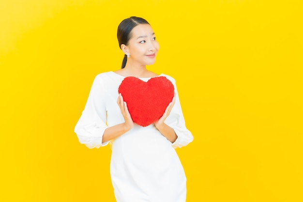 Sorriso di bella giovane donna asiatica del ritratto con la forma del cuscino del cuore su yellow