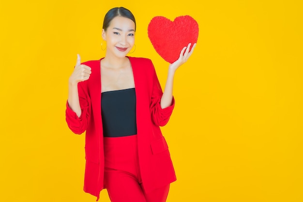 Sorriso di bella giovane donna asiatica del ritratto con la forma del cuscino del cuore su yellow