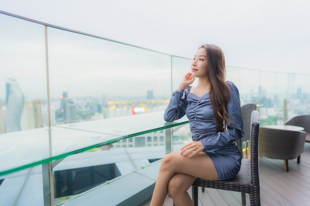 Sorriso felice della bella giovane donna asiatica del ritratto sul ristorante della cima del tetto intorno alla vista della città