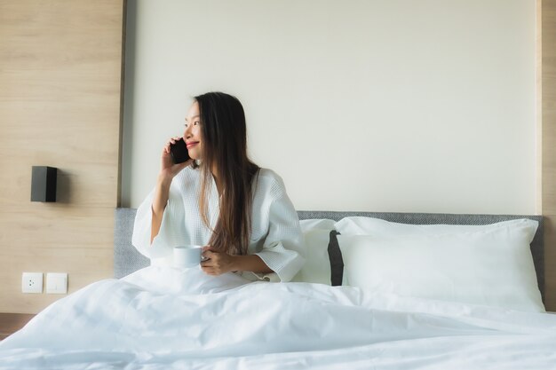 Sorriso felice delle belle giovani donne asiatiche del ritratto con caffè e il telefono cellulare