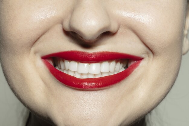 Sorriso felice. Tiro del primo piano della bocca femminile con trucco labbra rosso brillante e pelle delle guance ben tenuta.