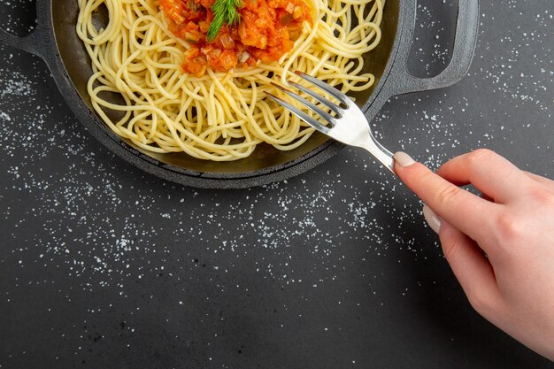 Spaghetti a metà vista superiore con salsa in padella forchetta in mano femminile su spazio libero tavolo nero