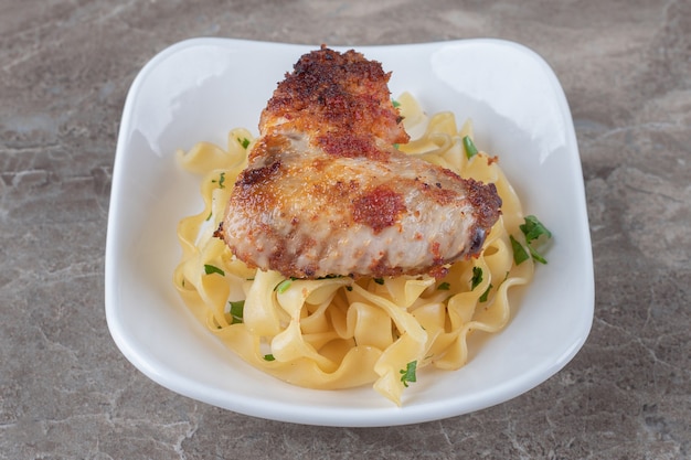 Spaghetti al wingover di pollo fritto alla piastra, sulla superficie di marmo.