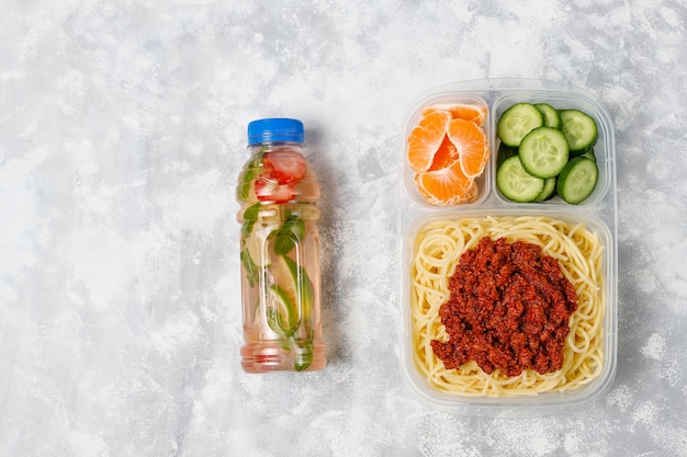 Spaghetti alla bolognese da asporto in una scatola da pranzo in plastica con bevanda disintossicante e fetta di frutta sulla luce