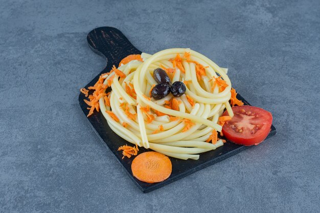 Spaghetti bolliti con verdure sul bordo nero.