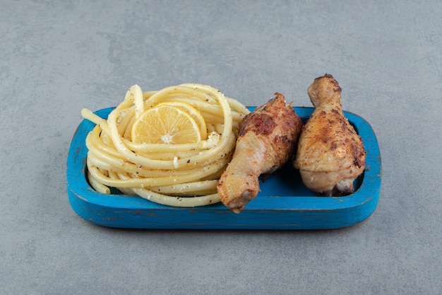 Spaghetti bolliti e cosce di pollo sul piatto blu.