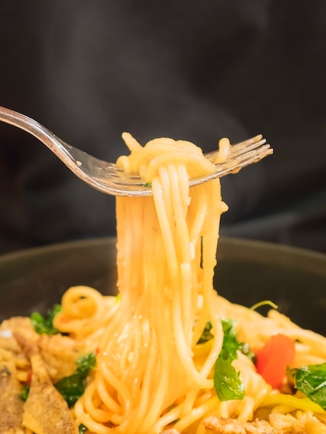 Spaghetti caldi e piccanti con forchetta su sfondo nero