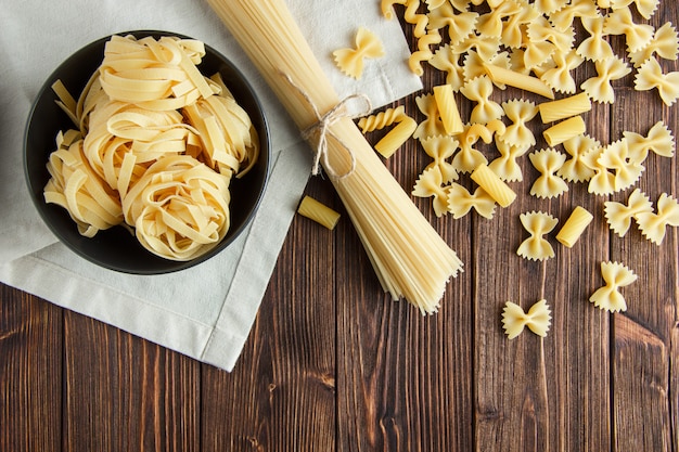 Spaghetti con pasta cruda assortita sul fondo dell'asciugamano di cucina e di legno, disposizione piana.