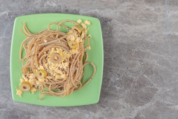 Spaghetti con uova fritte sul piatto verde.