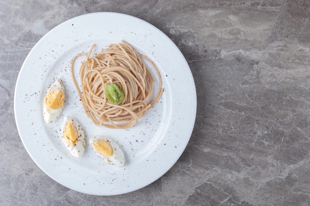 Spaghetti con uovo sodo sul piatto bianco.