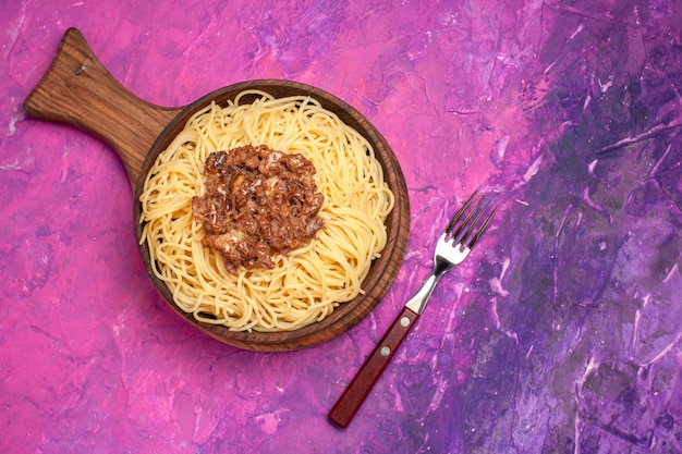 Spaghetti cotti vista dall'alto con carne macinata su condimento per pasta da tavola rosa