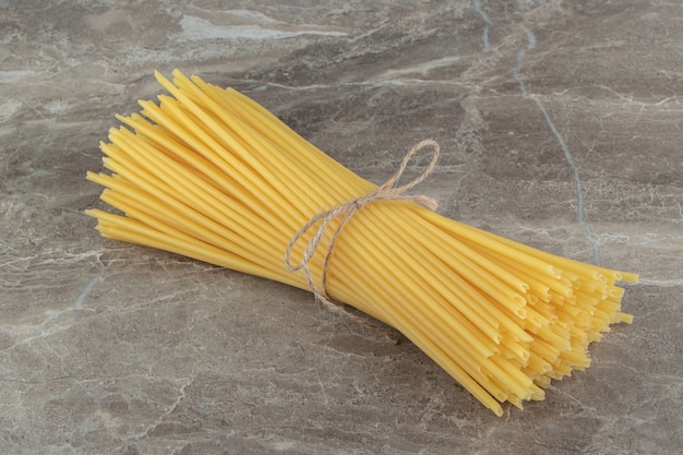 Spaghetti crudi del tubo legati con la corda sulla superficie di marmo