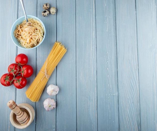 Spaghetti crudi e cucinati di vista superiore con i pomodori e l'aglio freschi su un fondo rustico di legno