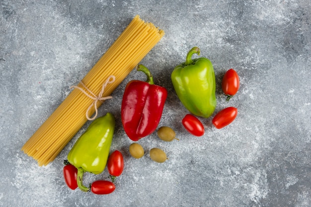 Spaghetti crudi e verdure varie sulla superficie della pietra.