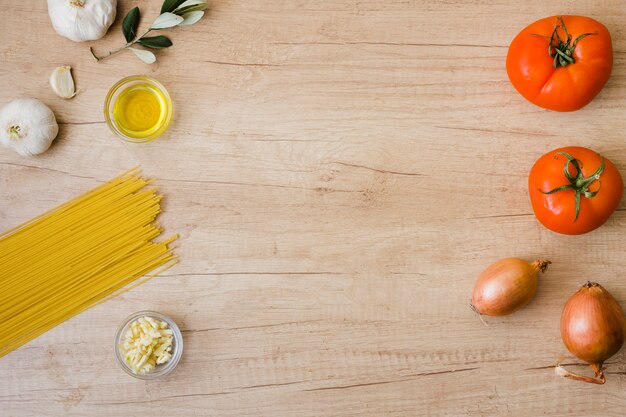 Spaghetti crudi; olio; aglio; cipolla e pomodori rossi sullo scrittorio di legno con lo spazio della copia per la scrittura del testo