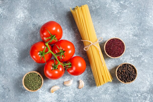 Spaghetti crudi, spezie e pomodori su fondo di marmo.