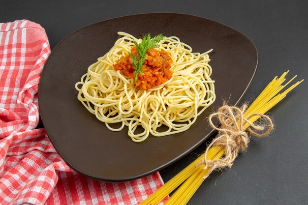 Spaghetti di vista dal basso con salsa sulla pasta cruda degli spaghetti del piatto sulla tavola nera