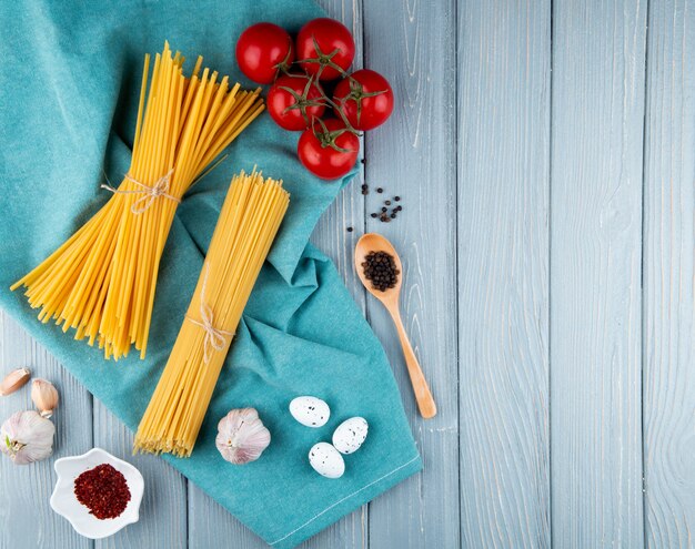 Spaghetti e linguini sullo spazio blu della copia di vista superiore delle uova dell'aglio del pomodoro del pepe del fondo